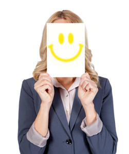 Blonde Frau, die sich ein Blatt Papier mit einem aufgezeichneten Smiley vor dem Gesicht hält.