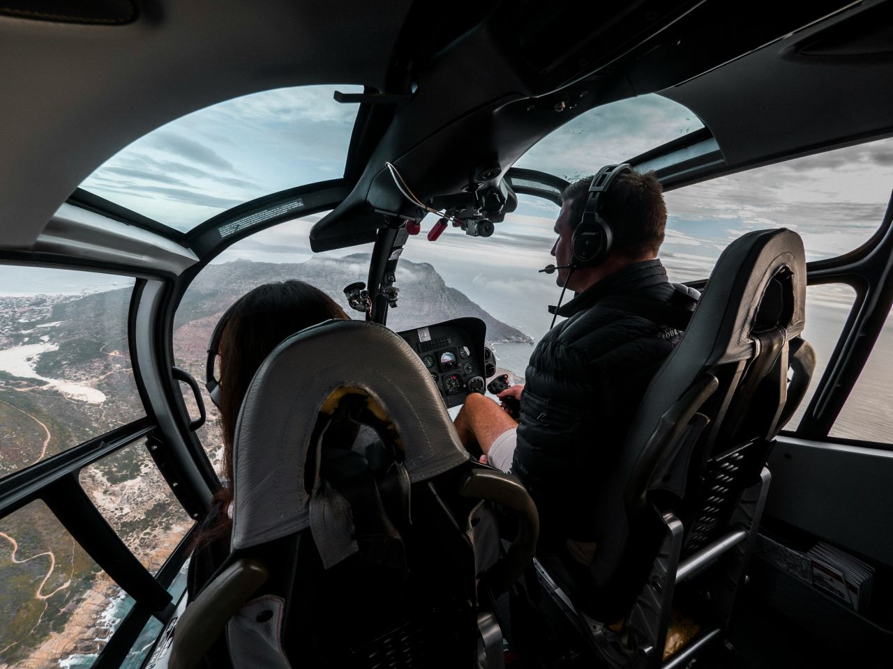 Foto von John O'Nolan auf Unsplash Zwei Piloten im Cockpit einer kleineren Maschine überfliegen eine Berglandschaft in Küstennähe.